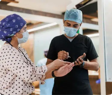 Healthcare professionals discussing patient information, wearing masks and surgical attire in a clinical setting.