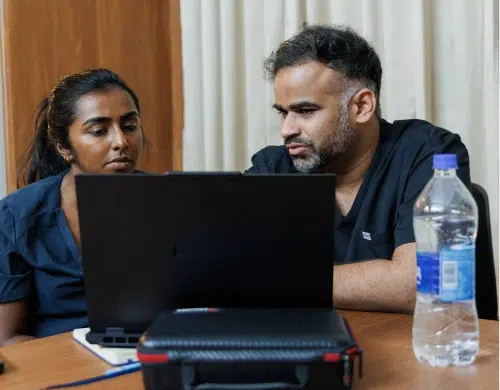 Specialist mentor and dentist consulting with a colleague over a laptop at a desk with a water bottle nearby.